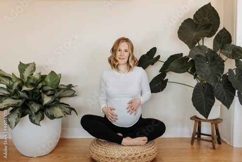 Pregnant woman sitting cross legged on hassock at home