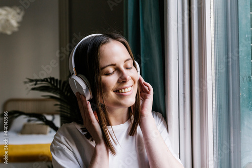 Woman smiling while listening music through headphones at home photo