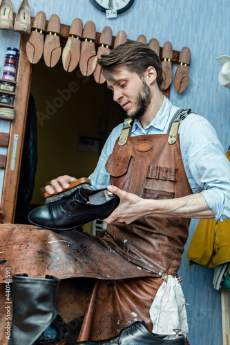 Male cobbler in apron polishing shoe with brush at workshop