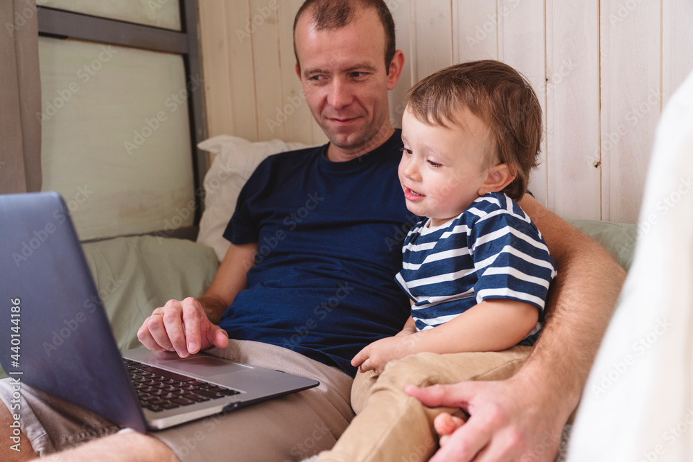 Father working on laptop while sitting with son at home office Father working on laptop while sitting with son at home office