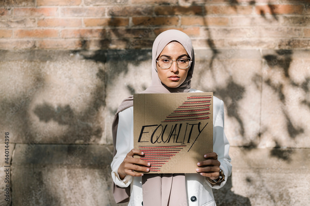 © Xavier Lorenzo/Westend61 - Young woman holding placard with equality text in front of wall on sunny day © Xavier Lorenzo/Westend61 - Young woman holding placard with equality text in front of wall on sunny day