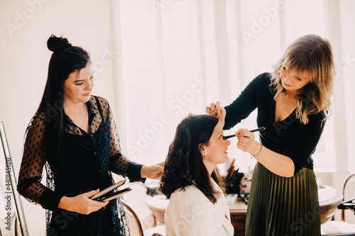 Female make-up artist and hairdresser preparing bride for wedding ceremony photo