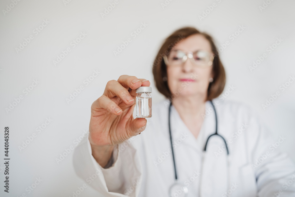 Senior female doctor holding vial in front of white wall Senior female doctor holding vial in front of white wall