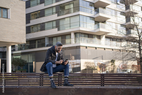 Smiling man using mobile phone while sitting on bench photo