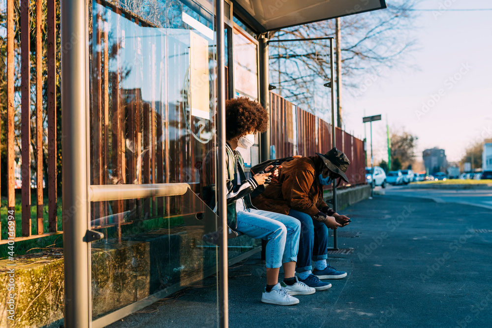 Women with protective face mask using mobile phone while sitting at bus station Women with protective face mask using mobile phone while sitting at bus station