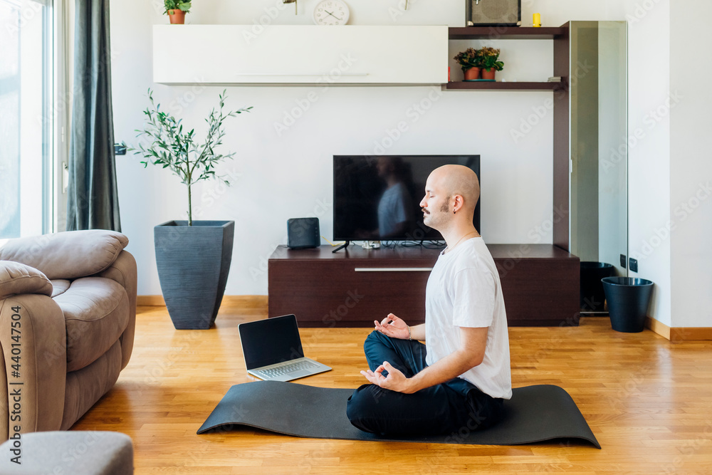 Bald man in lotus position sitting on exercise mat at home Bald man in lotus position sitting on exercise mat at home