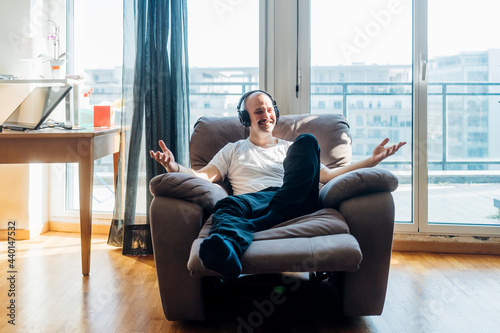 Smiling man wearing headphones gesturing while sitting on reclining chair in living room photo