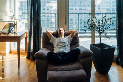 Young man with hands behind head relaxing on reclining chair at home photo