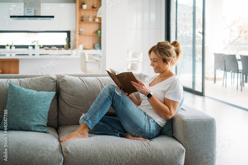 Female freelancer sitting on sofa while reading book at home photo