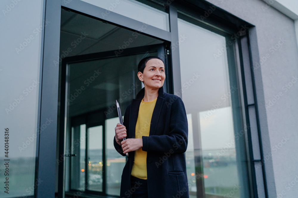 Smiling businesswoman looking away while holding laptop at doorframe Smiling businesswoman looking away while holding laptop at doorframe