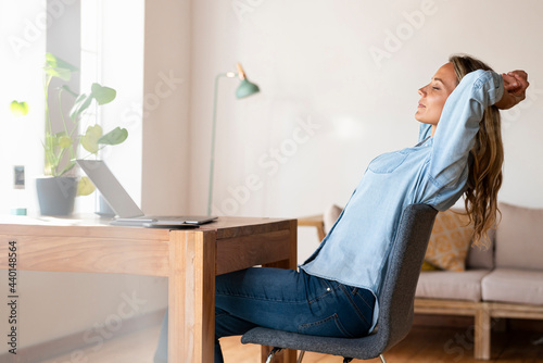 Relaxed female entrepreneur with eyes closed sitting in front of laptop at home photo