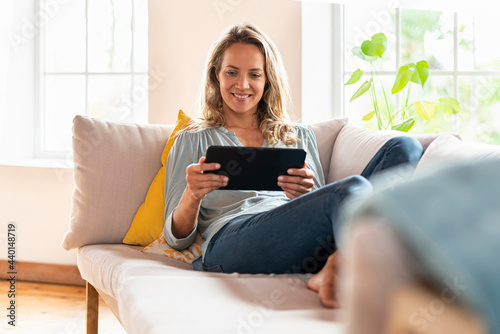 Contented woman looking at digital tablet while sitting on sofa in living room photo