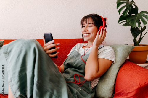 Smiling woman listening music while using mobile phone on sofa