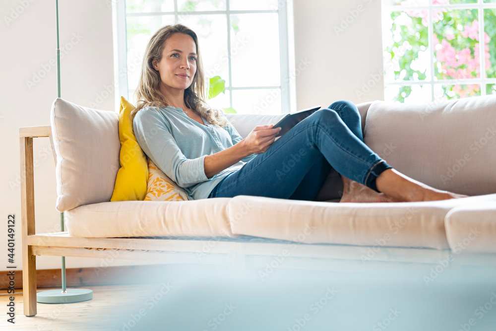 © steve brookland/Westend61 - Woman day dreaming while sitting with digital tablet on sofa © steve brookland/Westend61 - Woman day dreaming while sitting with digital tablet on sofa