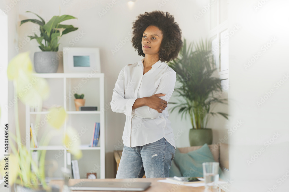 Thoughtful woman standing with arms crossed in living room Thoughtful woman standing with arms crossed in living room
