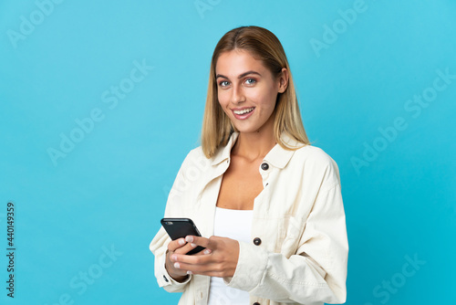 Young blonde woman isolated on blue background sending a message with the mobile