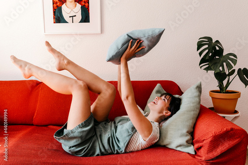 Happy woman playing with pillow while lying on sofa photo