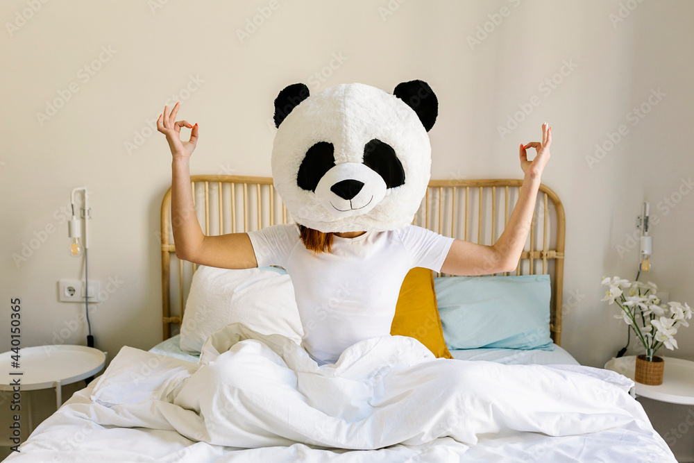 © Xavier Lorenzo/Westend61 - Woman wearing panda mask meditating on bed at home