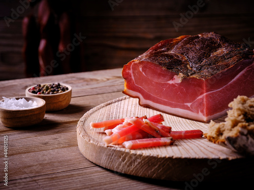 Bacon from pork loin on wooden board with salt and pepper in bowls and piece of bread photo