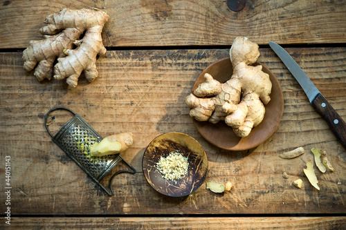 Kitchen knife, ginger roots and old grater lying on wooden surface photo