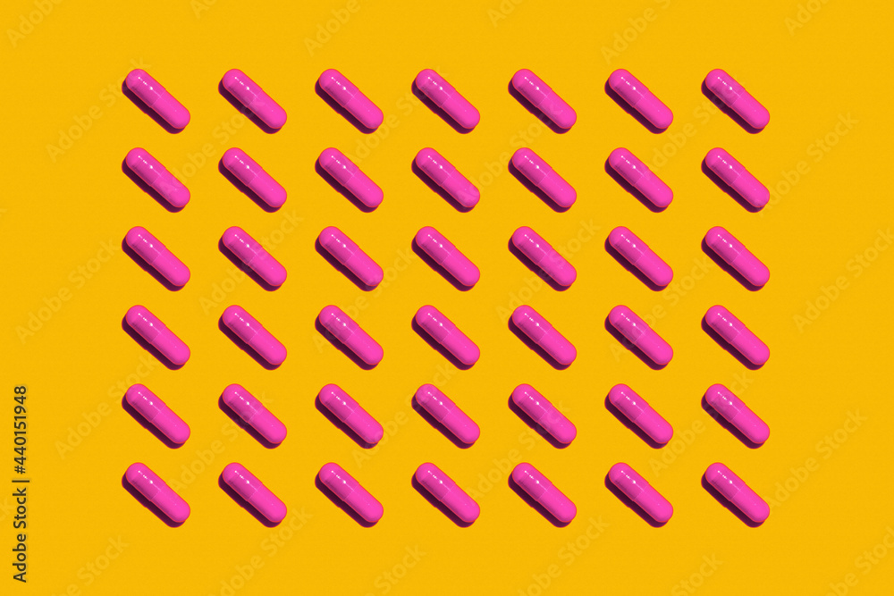 Pattern of rows of pink medicine capsules laid against yellow background