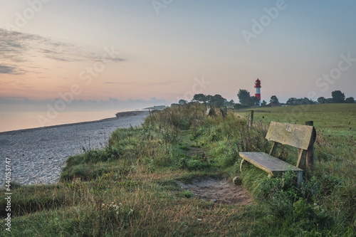 Germany, Schleswig-Holstein, Pommerby, Empty beachside bench at dusk with Falshoft lighthouse in background photo