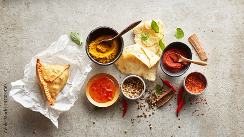 Studio shot of samosa dumpling on paper napkin, masala spices, chili dipping sauce, naan bread and red chili peppers photo