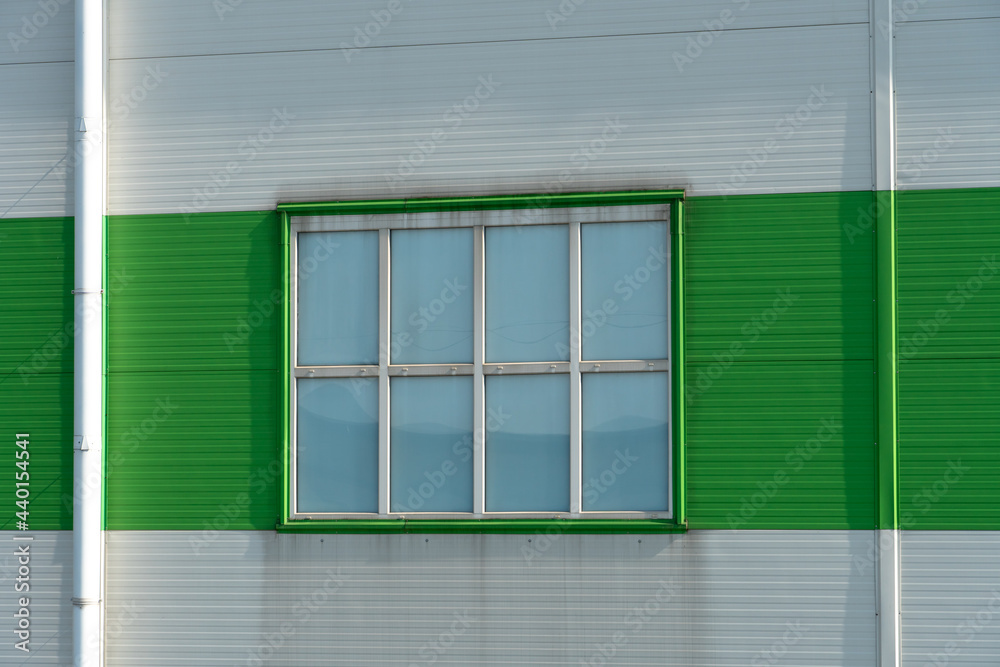 Fototapeta premium a window in the wall of a modern factory or a large shopping center. Details of the aluminum facade of an industrial building. The building is made of corrugated aluminum plates of green and white