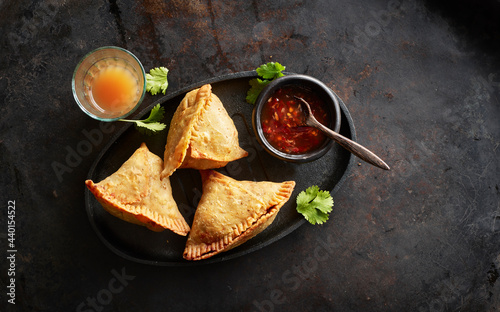 Tray with samosa dumplings, bowl of chili sauce and glass of chai tea photo