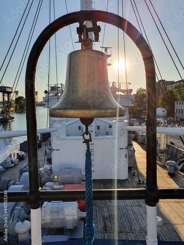 Bell aboard the ship. Bright rays of the sun shine on the deck.