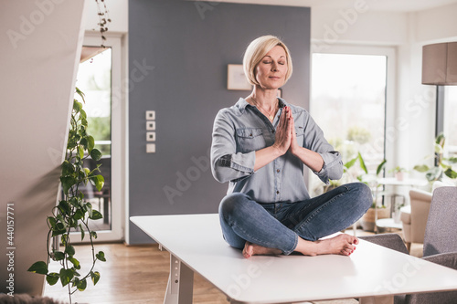 Mature woman meditating while sitting on table at home photo