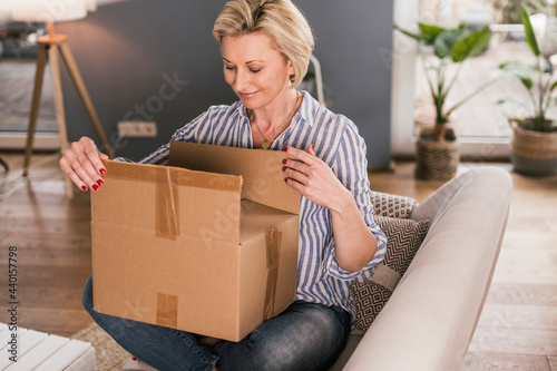 Smiling mature woman opening package while sitting on sofa at home