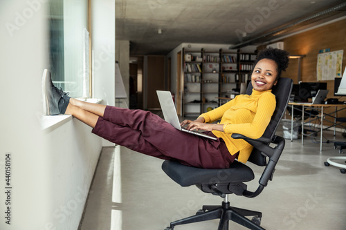 Smiling female professional with laptop looking away while sitting on chair at office