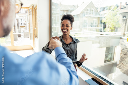 Smiling female professional doing fist bump with male colleague in office photo