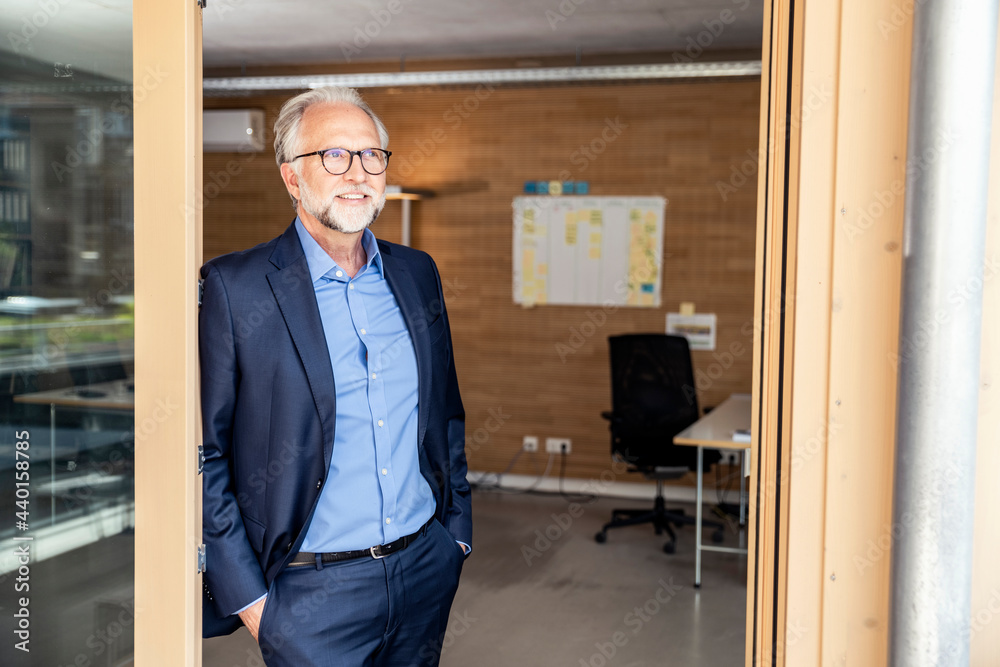 Mature businessman looking away while leaning on doorframe at office Mature businessman looking away while leaning on doorframe at office