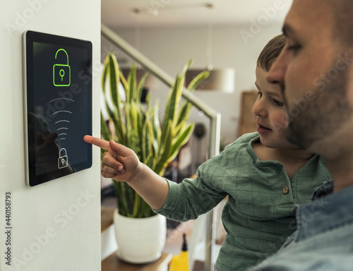 Father carrying son pointing at security tablet in smart home photo