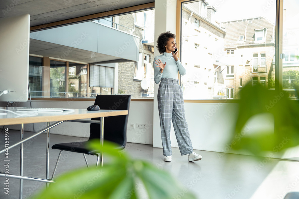 © Uwe Umstatter/Westend61 - Smiling businesswoman gesturing while talking on mobile phone by window at office © Uwe Umstatter/Westend61 - Smiling businesswoman gesturing while talking on mobile phone by window at office
