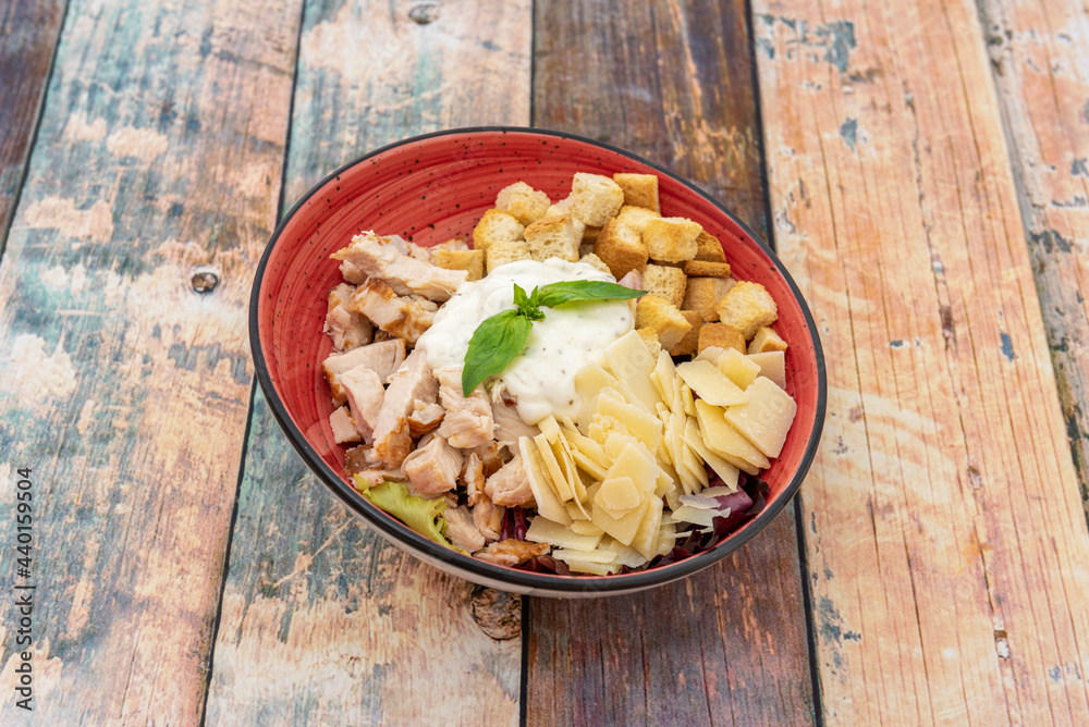 Amazing caesar salad with lots of flaked parmesan cheese, chicken pieces, mayonnaise and croutons inside a red bowl Amazing caesar salad with lots of flaked parmesan cheese, chicken pieces, mayonnaise and croutons inside a red bowl