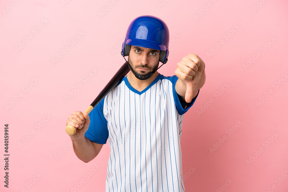 Baseball player with helmet and bat isolated on pink background showing thumb down with negative expression