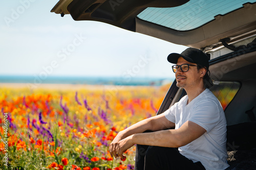Man sitting in car by colorful meadow in summer