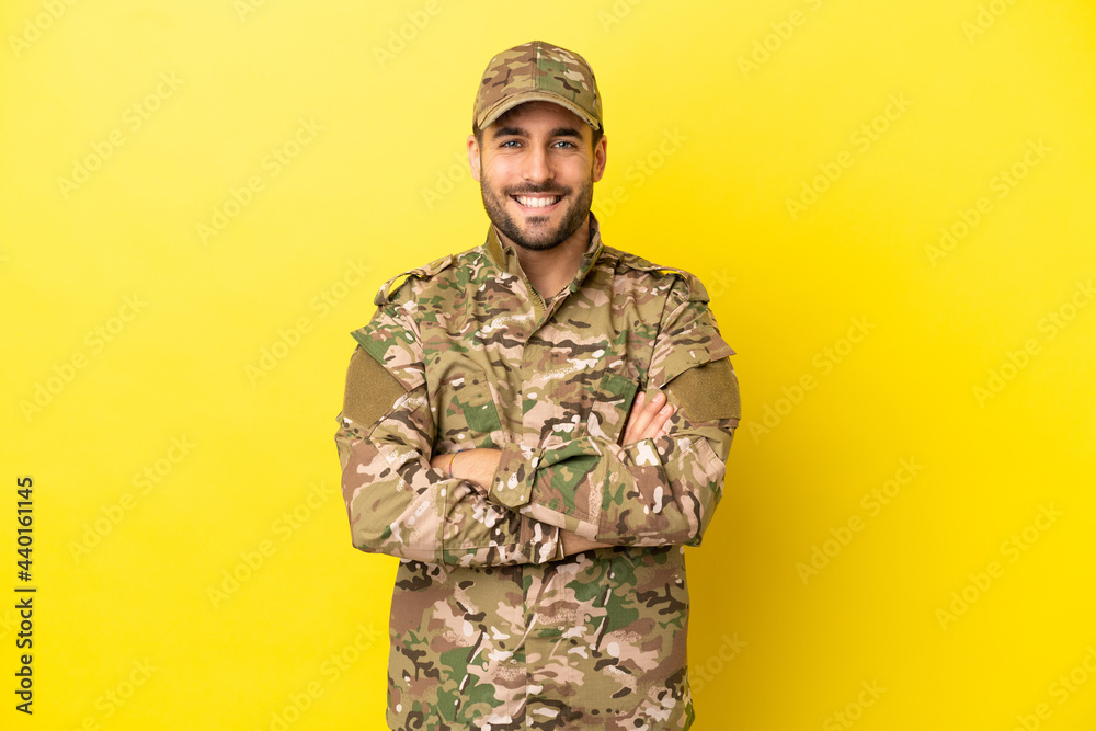 Military man isolated on yellow background keeping the arms crossed in frontal position Military man isolated on yellow background keeping the arms crossed in frontal position