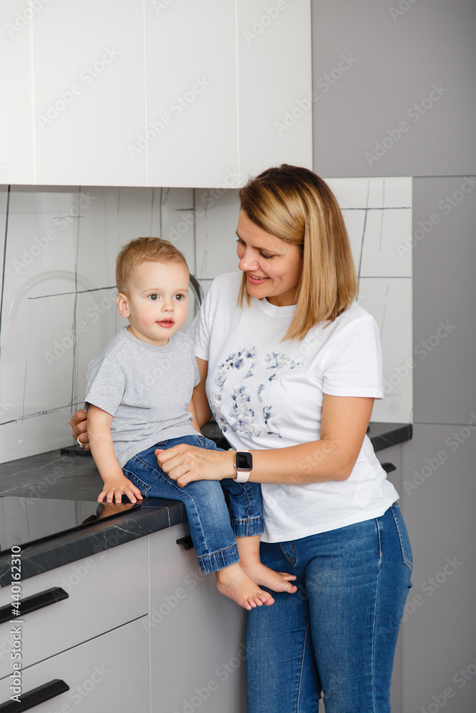 Happy family in casual denim in a kitchen room. Little boy with his mother at home. Good morning parent and infant son in jeans wear. Family weekdays traditions. Relationship with love Happy family in casual denim in a kitchen room. Little boy with his mother at home. Good morning parent and infant son in jeans wear. Family weekdays traditions. Relationship with love