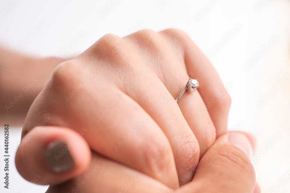 closeup of the hands of a couple touching each other, she has an engagement ring, they are on a white background, concept of marriage proposal.