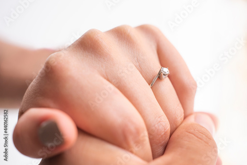 closeup of the hands of a couple touching each other  she has an engagement ring  they are on a white background  concept of marriage proposal.
