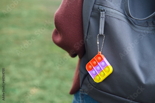 Rainbow bubble pop it fidget toy hanging on the backpack. For autistic patients to relieve stress, help restore mood. Squeeze sensory game. Simple dimple. Push pop for homeschool or office. photo