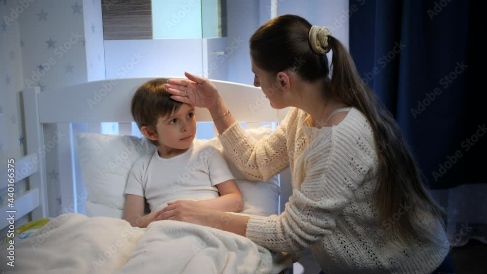 Young caring mother touching forehead of her sick little son lying in bed. Concept of children illness, disease and parent care Young caring mother touching forehead of her sick little son lying in bed. Concept of children illness, disease and parent care