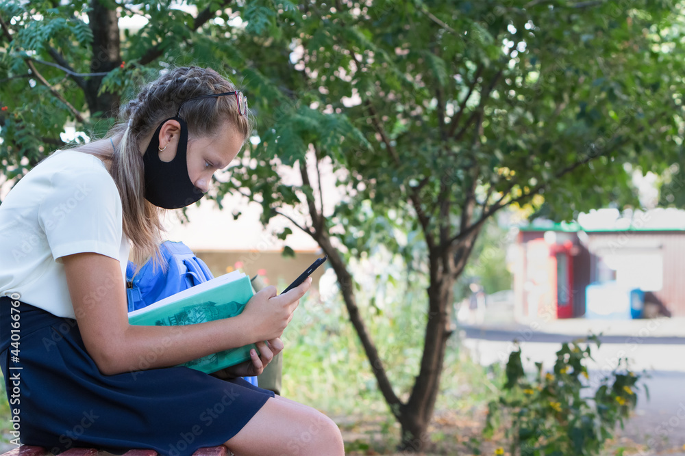 Schoolgirl girl on the street with a textbook and in a protective mask. Schoolgirl girl on the street with a textbook and in a protective mask.