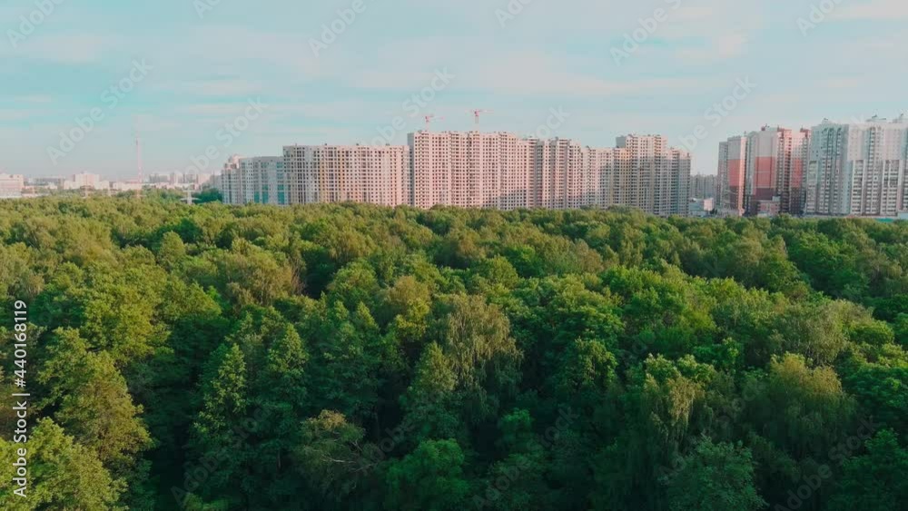 Drone flies over park towards huge housing estates under construction at sunset, construction cranes, green trees, St. Petersburg, Russia Drone flies over park towards huge housing estates under construction at sunset, construction cranes, green trees, St. Petersburg, Russia