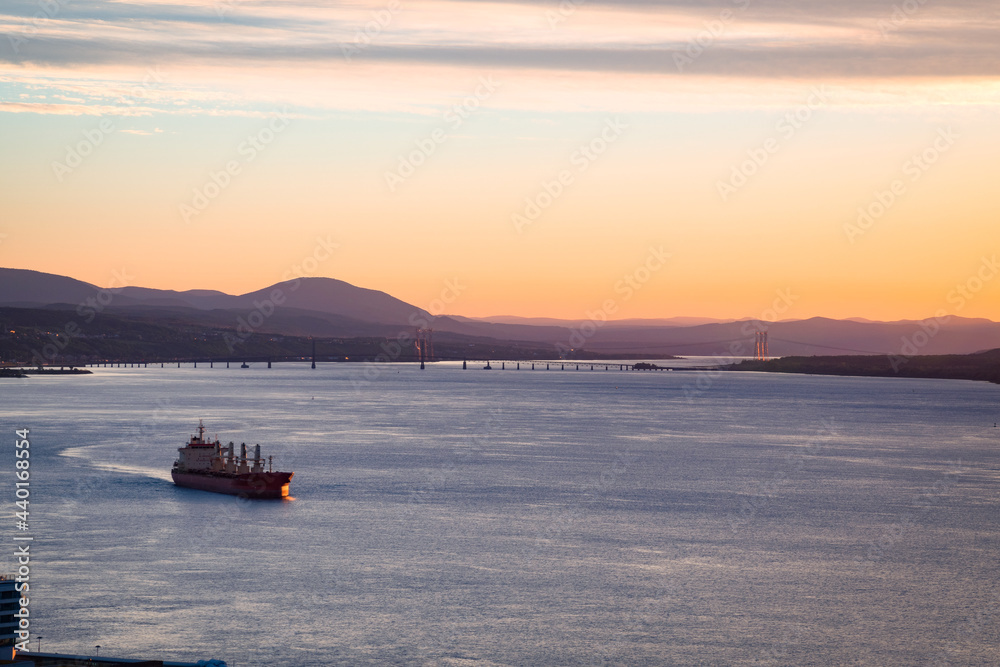 Obraz premium A freight ship navigating through St-Lawrence river at sunrise, with majestic landscape in background, Quebec city harbor, Canada