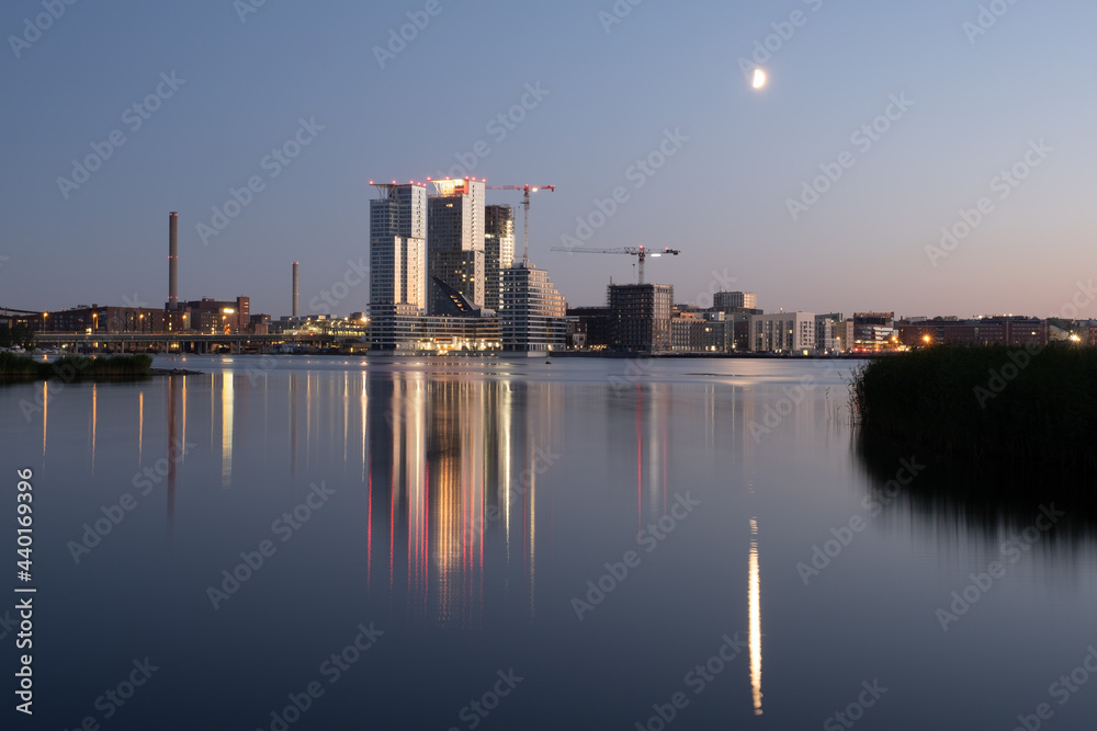 Beautiful modern city skyline on the waterfront during midsummer evening. Buildings casting reflections on the water.